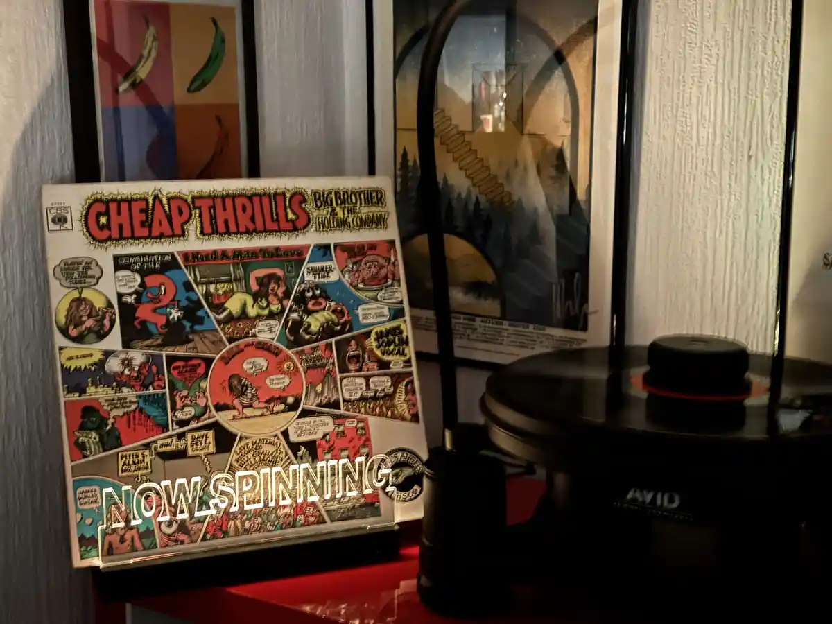 A vinyl record album cover for 'Cheap Thrills' by Big Brother & The Holding Company is displayed upright next to a record…