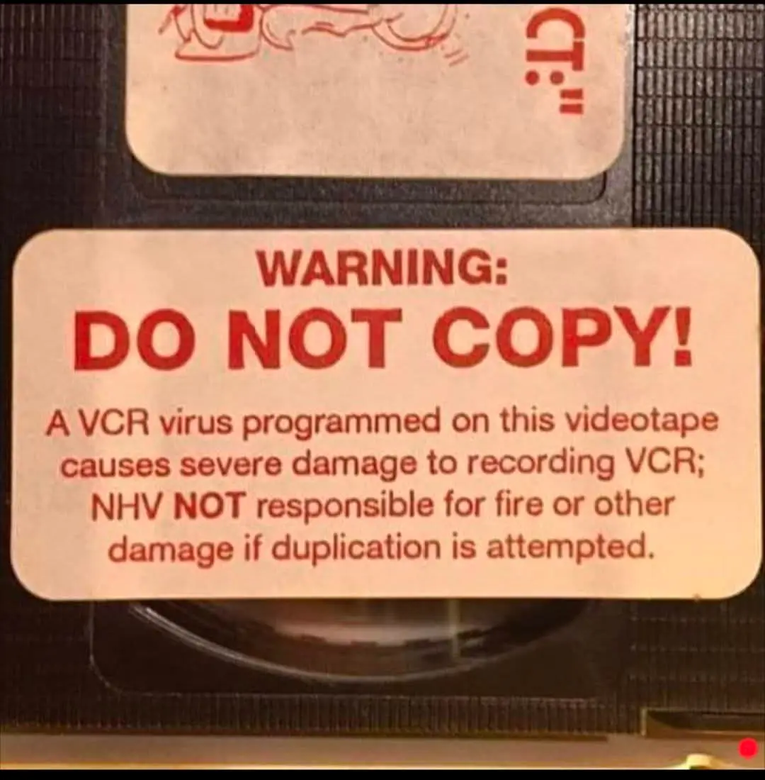 A close-up of a VHS tape label with a red warning sticker that reads 'WARNING: DO NOT COPY!' followed by text claiming a…