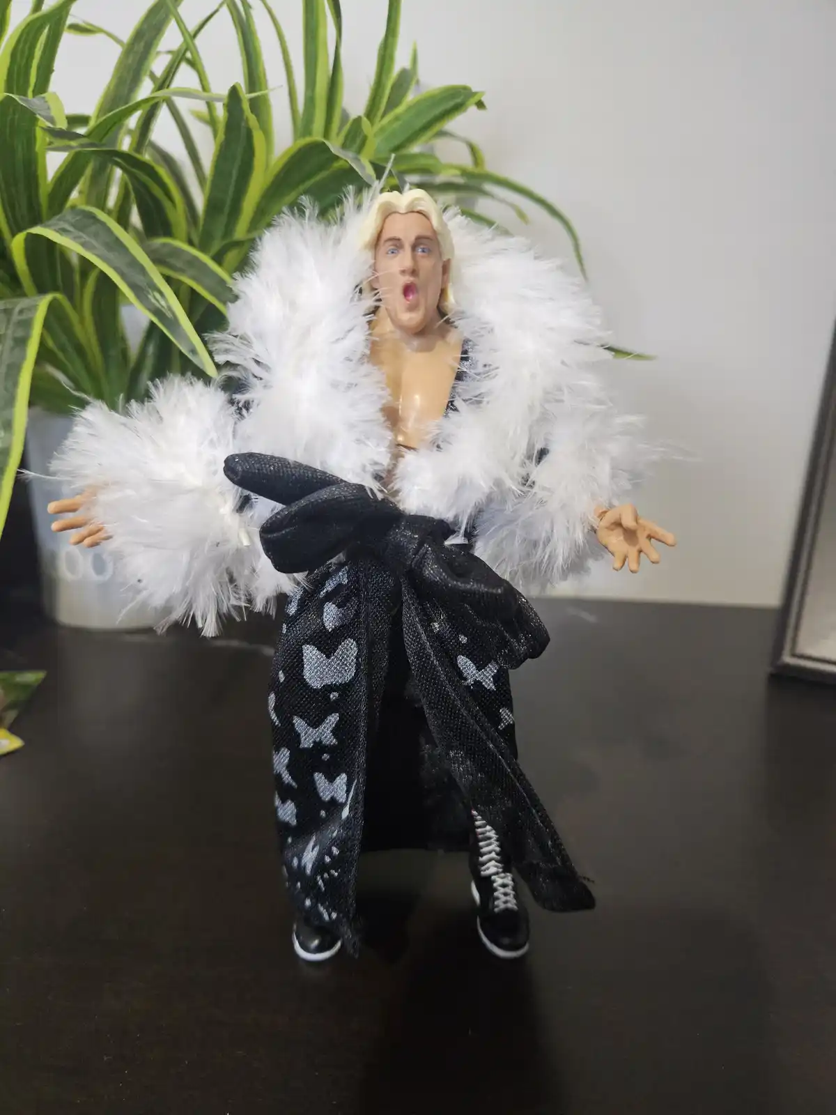 A plastic action figure of a blonde man with a shocked expression, wearing a black robe with white butterfly patterns and a…