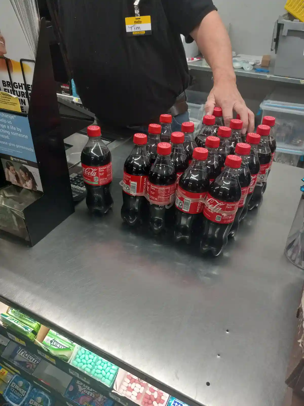 A cashier named Tim, identifiable by his name tag, is at a Dollar General checkout counter arranging a large pack of…