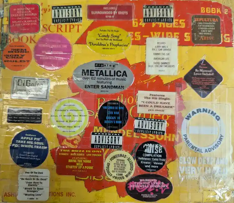 A collage of fake cassette tape labels pasted on a yellow surface, featuring absurdly exaggerated album titles and…