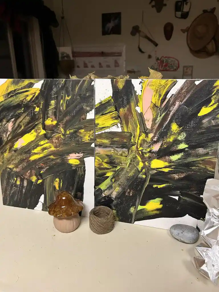 Two abstract paintings with thick yellow, black, and green brushstrokes are displayed side by side on a white surface. In…