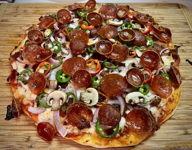 A close-up photo of a heavily loaded pizza on a wooden cutting board, covered with pepperoni, green and red bell peppers…