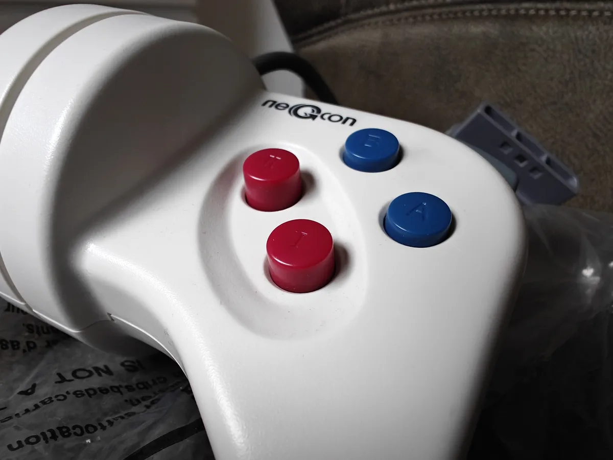 A close-up photo of a white neGcon game controller with two red buttons labeled 'I' and one blue button labeled 'A', and…