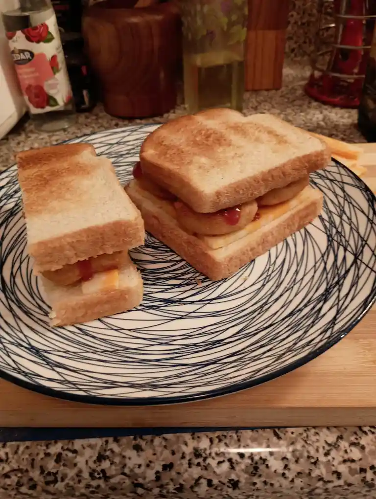 A homemade sandwich on toasted white bread, cut in half and stacked on a blue and white patterned plate, with visible layers…