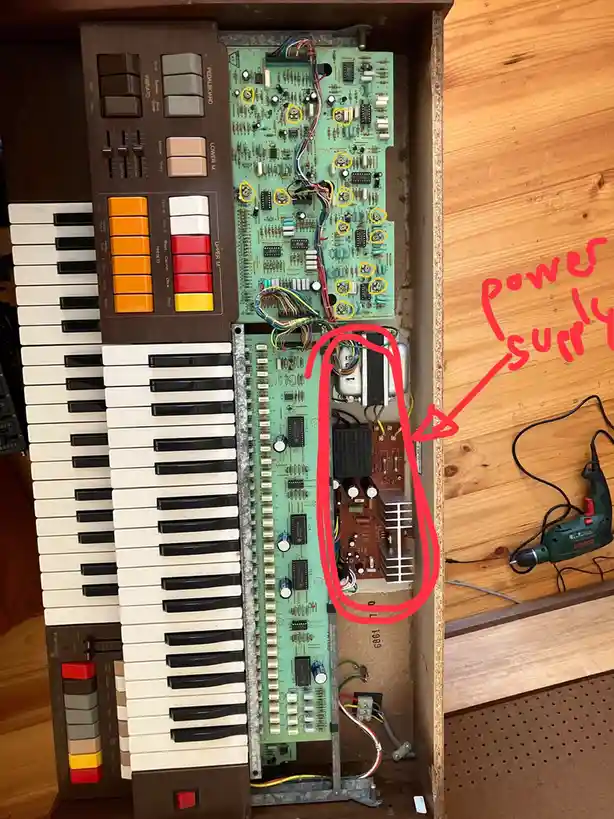 An image shows the inside of a vintage keyboard with exposed circuit boards and wiring. A red hand-drawn arrow points to a…