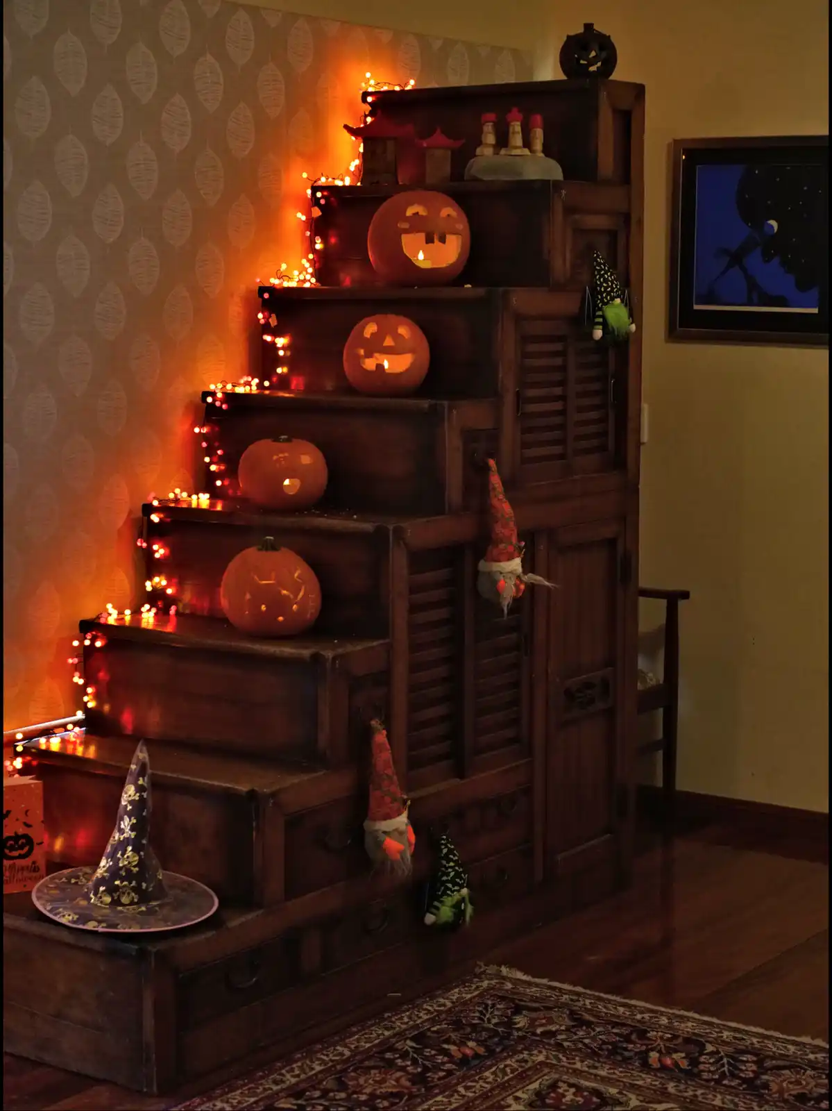 A dark wooden cabinet is decorated with multiple carved pumpkins, some lit from within, and adorned with string lights…