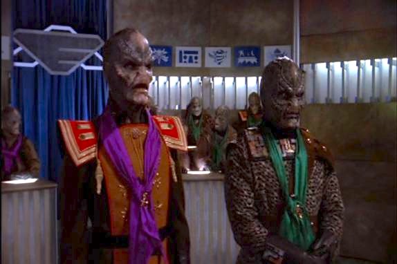 Two alien characters from the Star Trek universe, likely Klingons, stand side by side in what appears to be a formal or…
