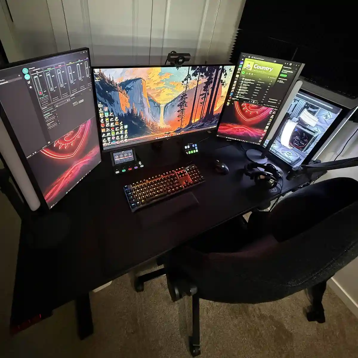 An overhead view of a high-end gaming or streaming setup with four monitors on a black desk, featuring a keyboard, mouse…