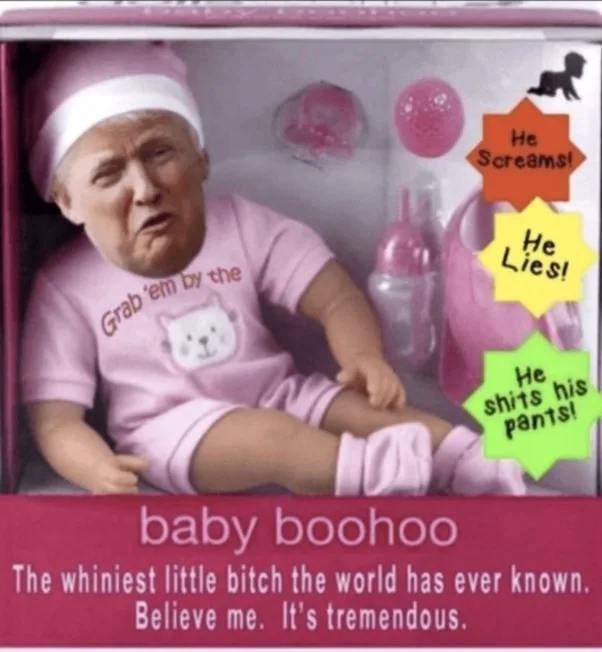 A baby doll packaged in a pink box, featuring a superimposed image of Donald Trump's face. The doll wears a pink onesie with…