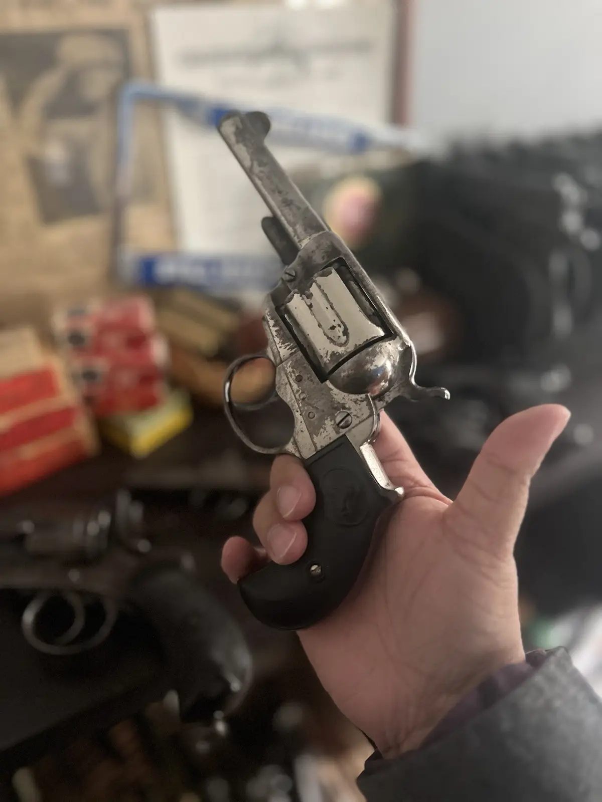 A hand holds a small, worn revolver with a black grip and silver barrel, showing its open cylinder. The background is…