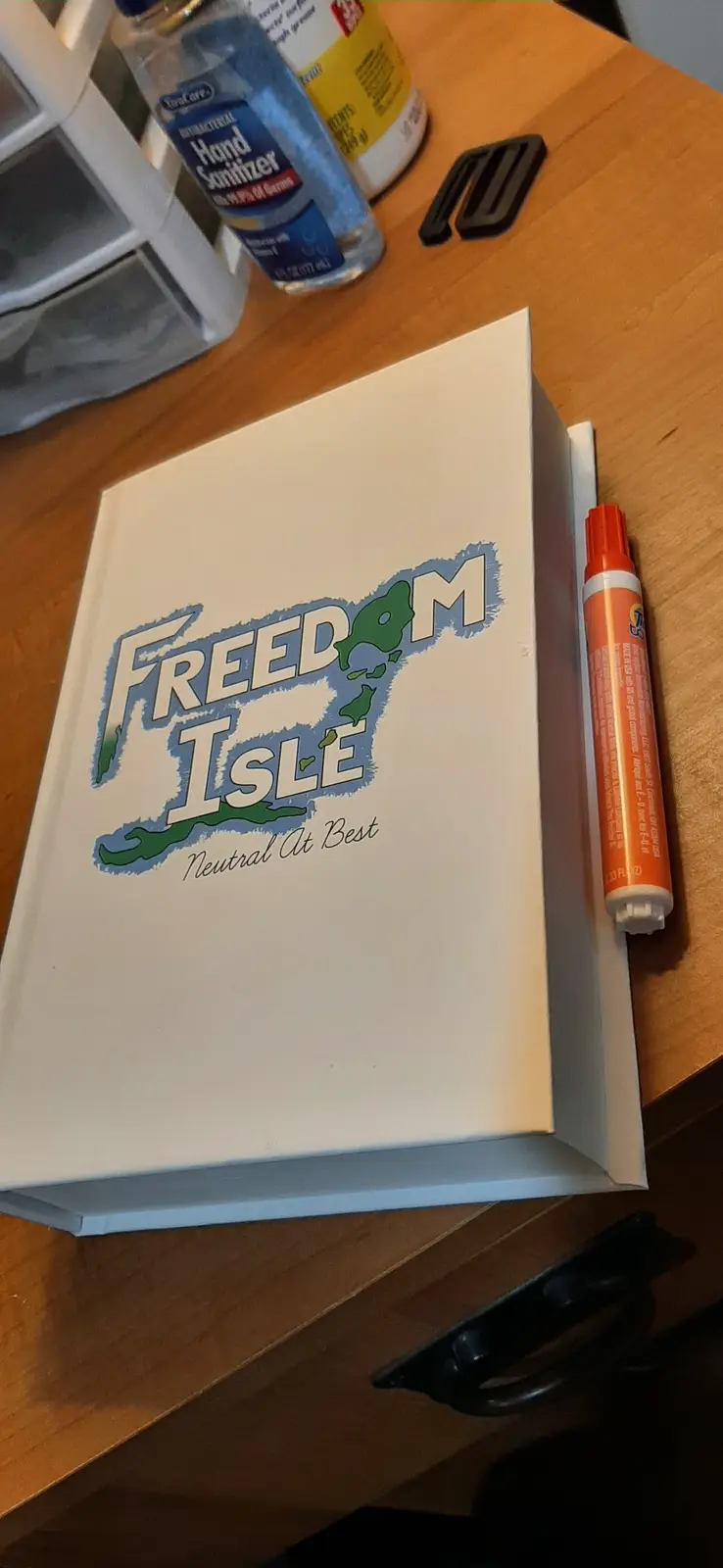 A white box sits on a wooden table with a logo that reads 'FREEDOM ISLE' in stylized lettering, with the shape of an island…