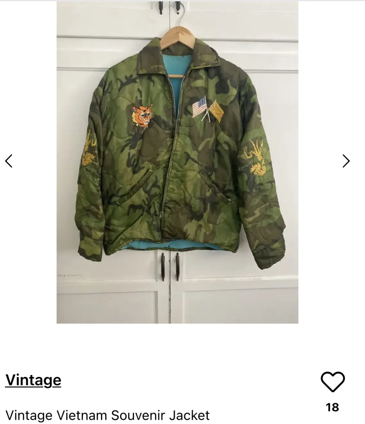 A vintage green camouflage quilted jacket hangs on a wooden hanger against a white paneled wall. It features embroidered…