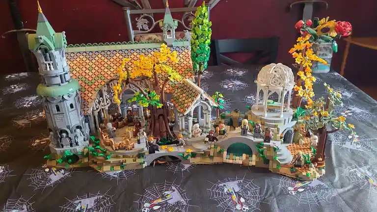 A detailed LEGO model of Hobbiton from The Lord of the Rings, featuring a large house with a tower, a garden with trees and…