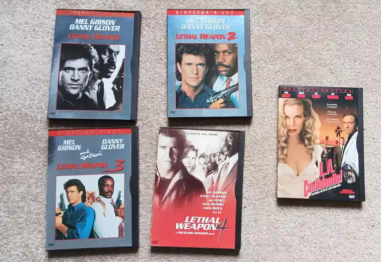 Five DVD cases are laid out on a carpeted floor: four 'Lethal Weapon' movies (1-4) featuring Mel Gibson and Danny Glover…