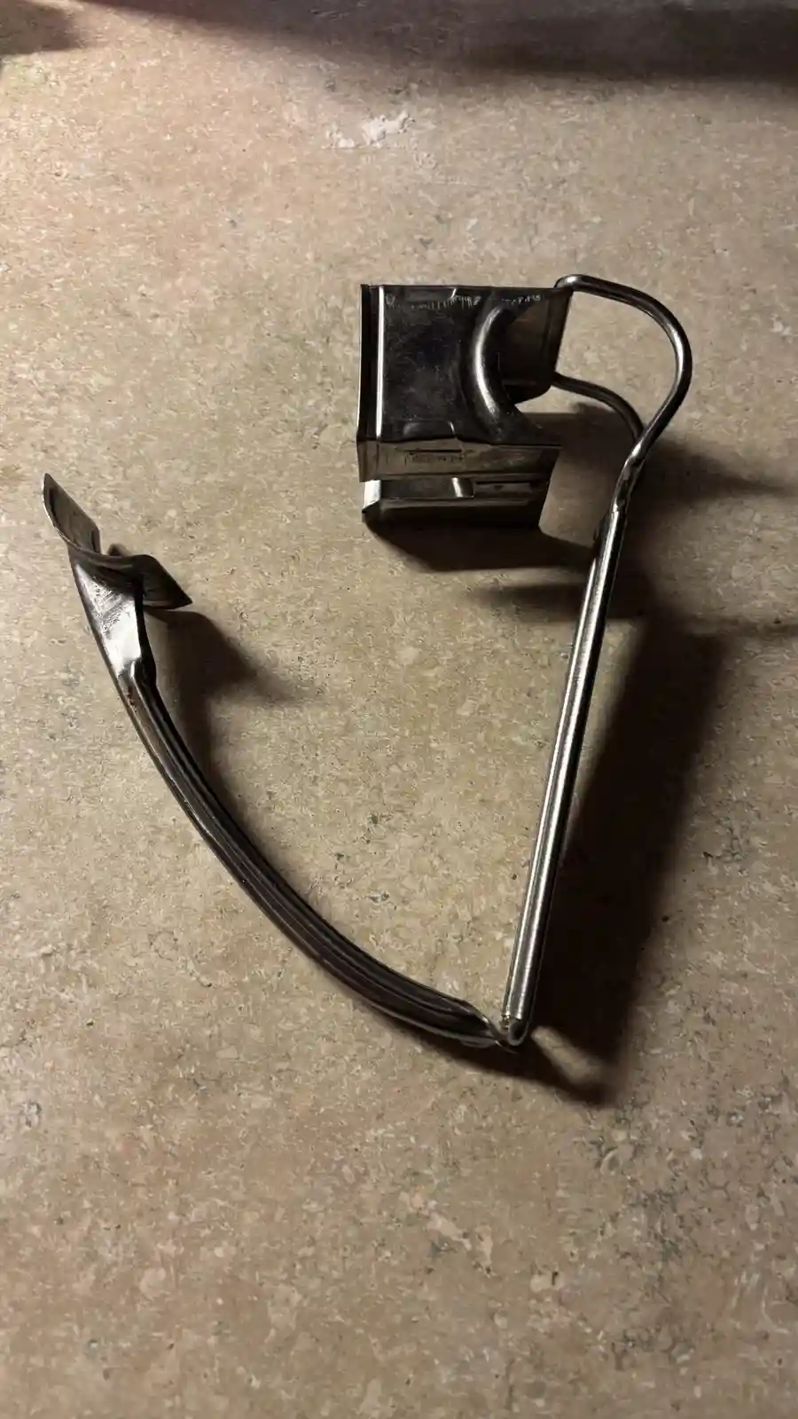 A broken pair of metal-framed glasses lies on a speckled countertop, with one arm detached and the other bent, visually…