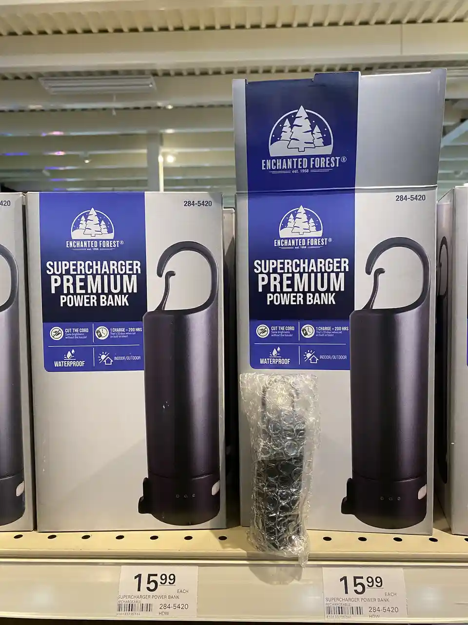 Two boxes of 'Enchanted Forest' branded 'Supercharger Premium Power Bank' sit on a store shelf, priced at $15.99 each. One…