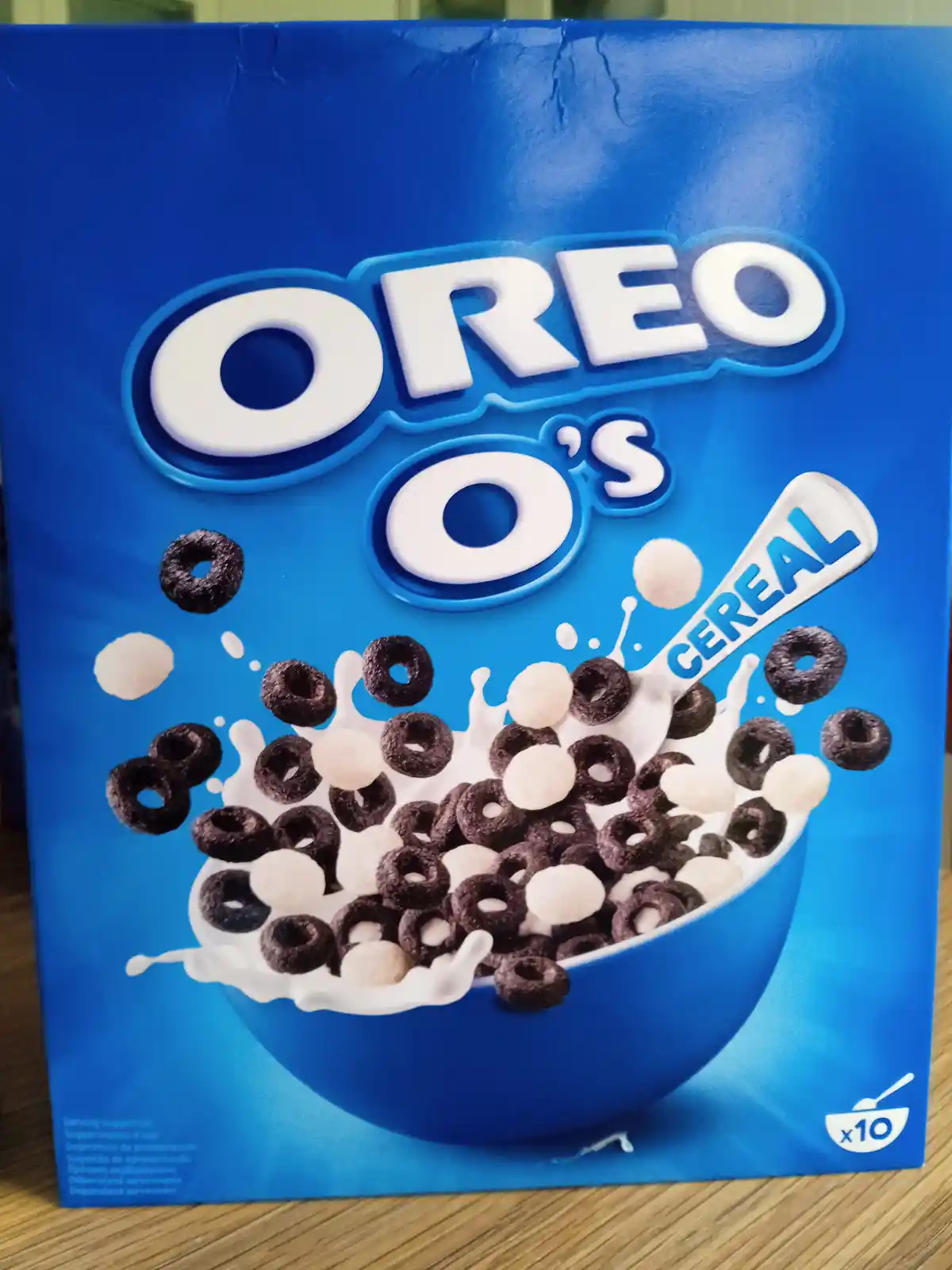 A blue cereal box labeled 'OREO O's CEREAL' shows a bowl of chocolate ring cereal mixed with white cereal pieces and milk…