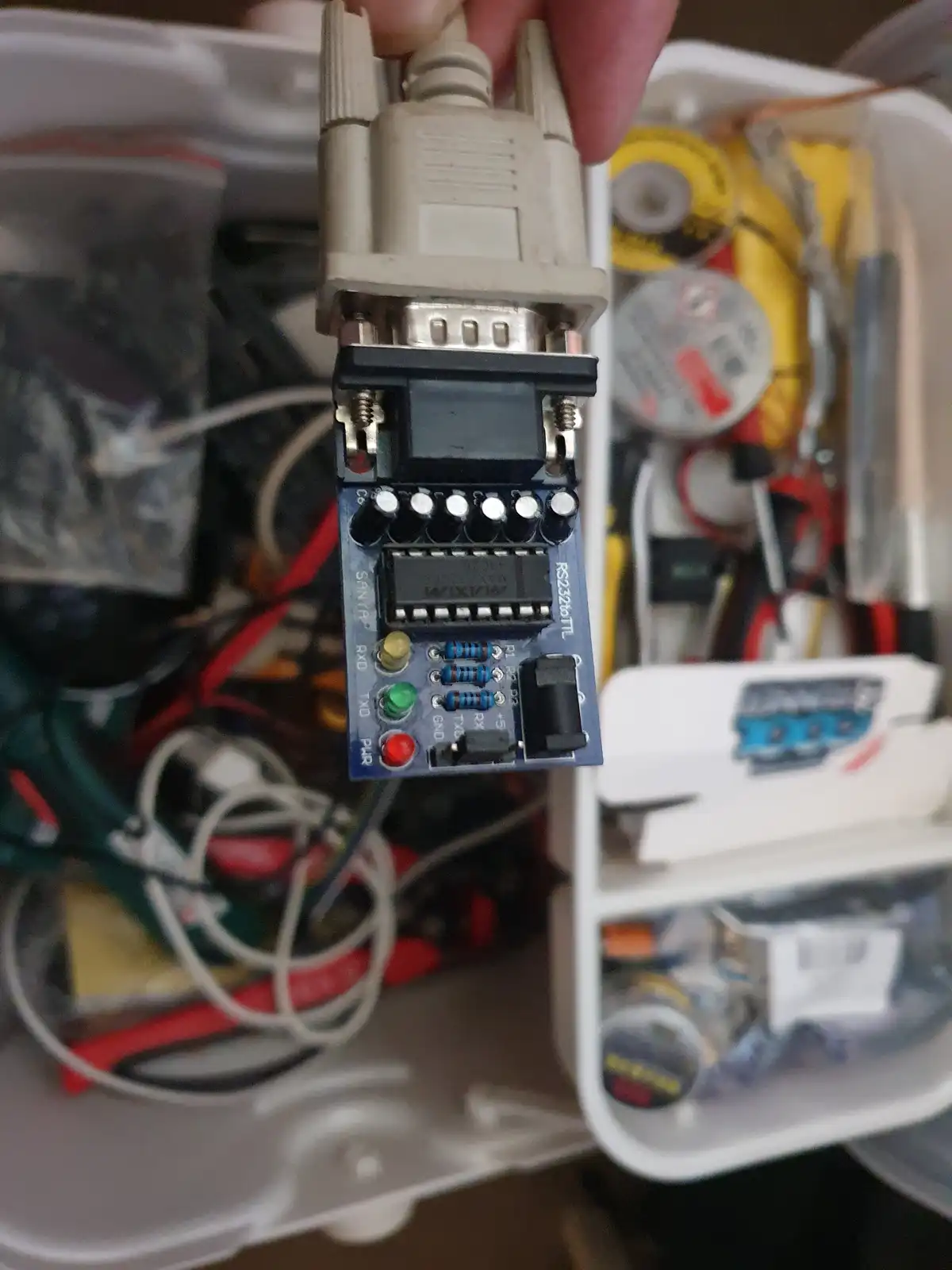A hand holds a custom-built electronic adapter with a DB9 serial port connector on top and a USB connector on the bottom…