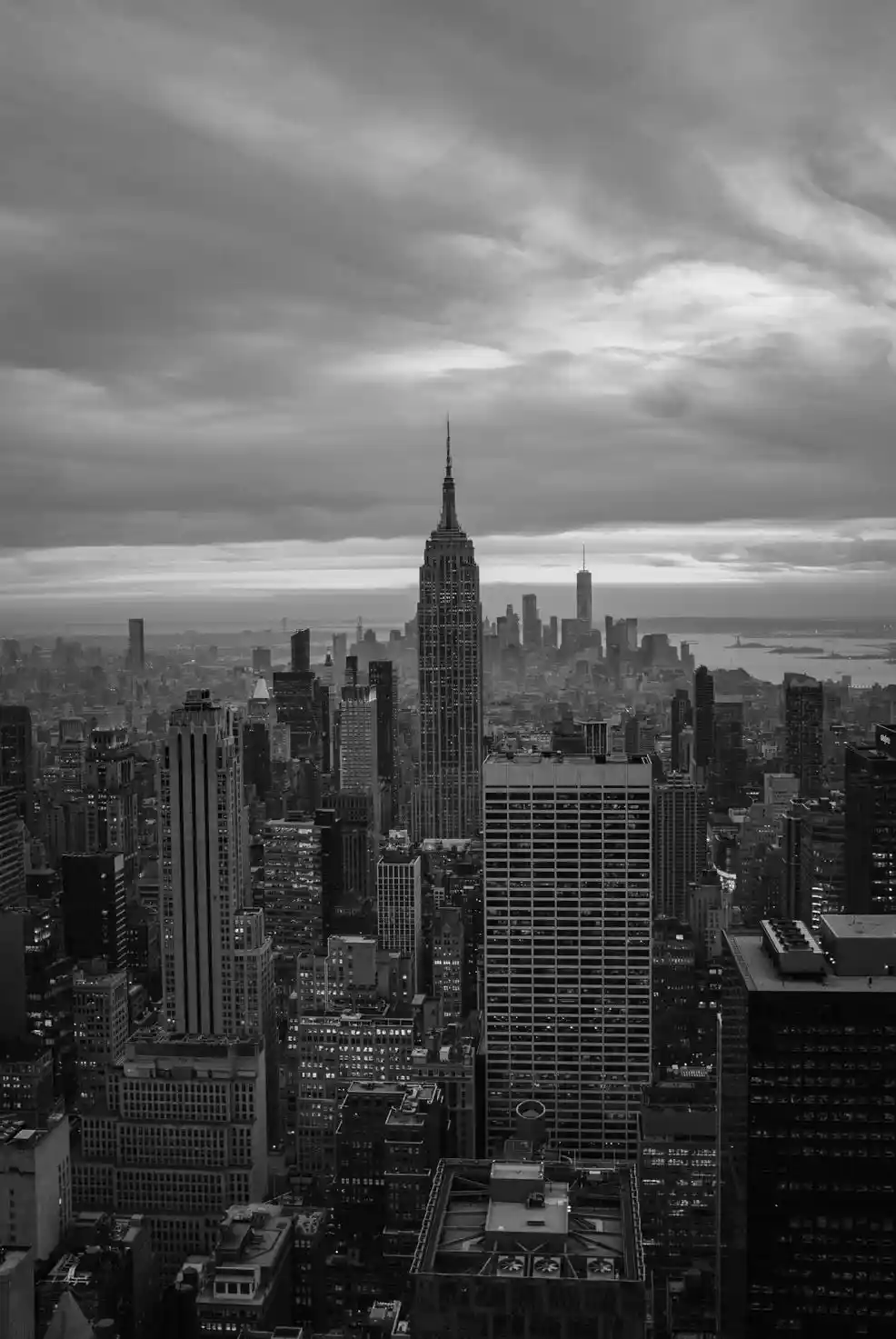 A black-and-white photograph of the New York City skyline, prominently featuring the Empire State Building at its center…