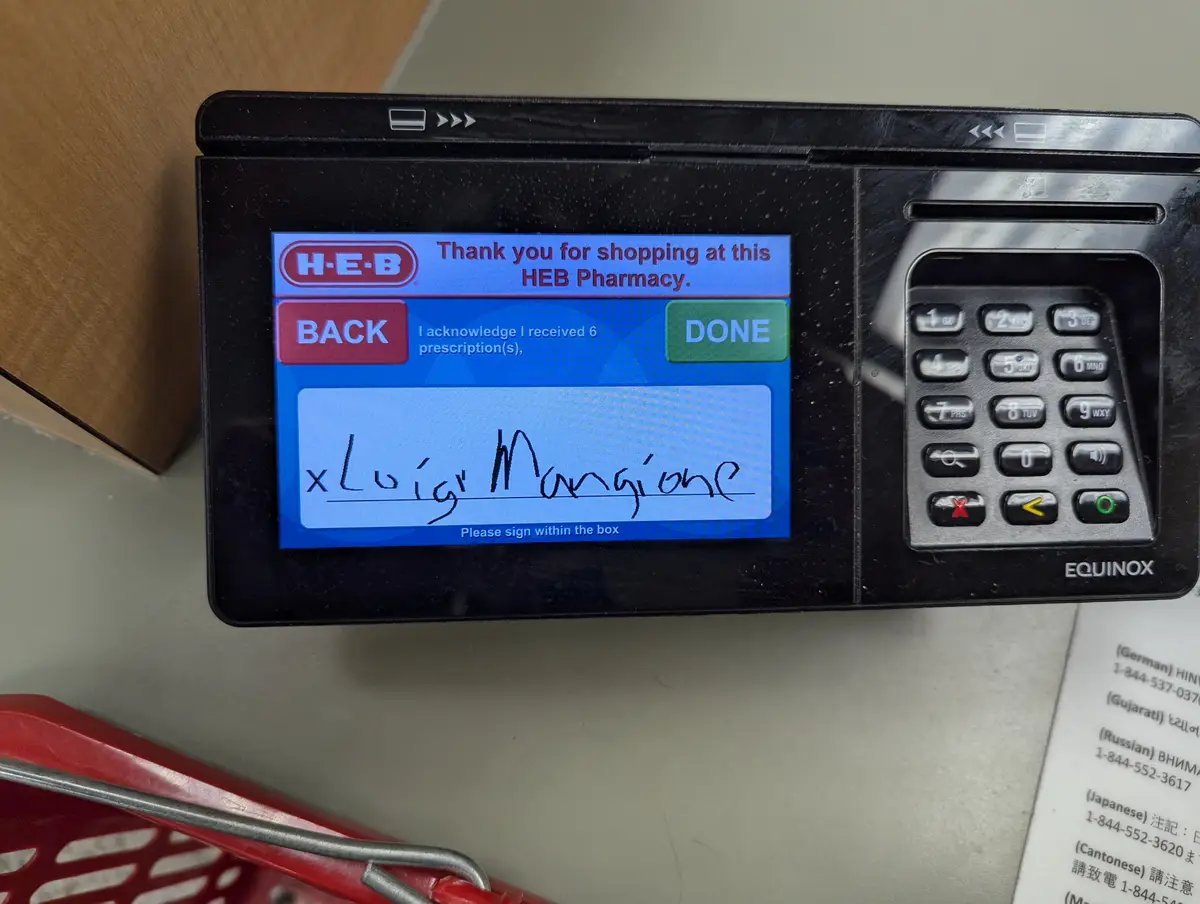 A close-up photo of an H-E-B pharmacy kiosk screen showing a signature pad with the handwritten name 'Luigi Mangione' next…
