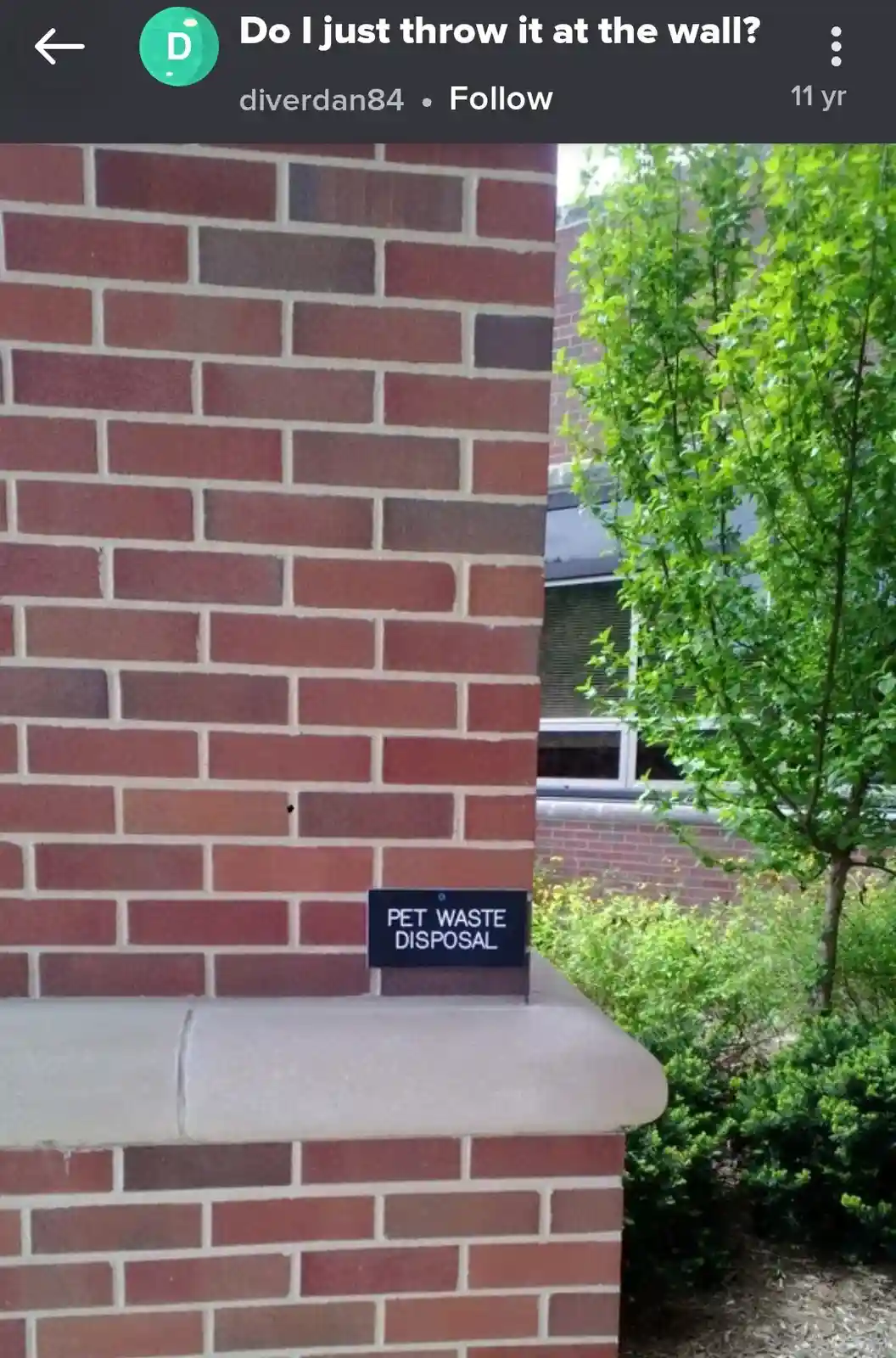 A close-up photo shows a small black sign reading 'PET WASTE DISPOSAL' mounted on a red brick pillar. The pillar has a…