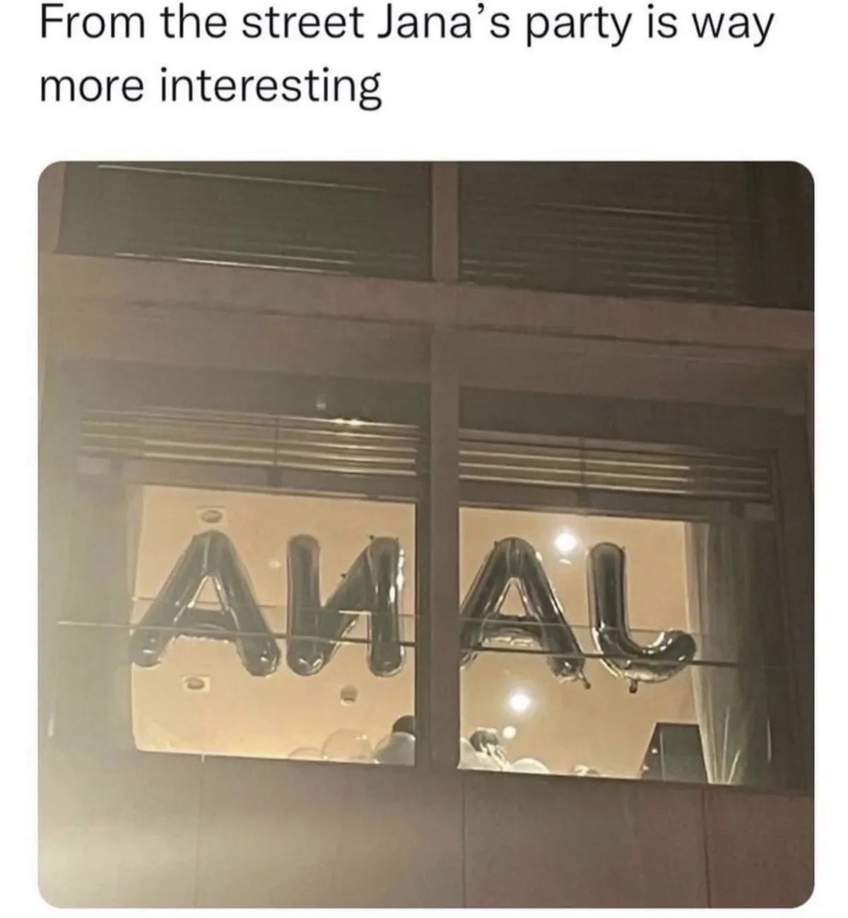 A nighttime photo shows large, shiny black balloon letters spelling 'ANAL' across two windows of a building, viewed from the…
