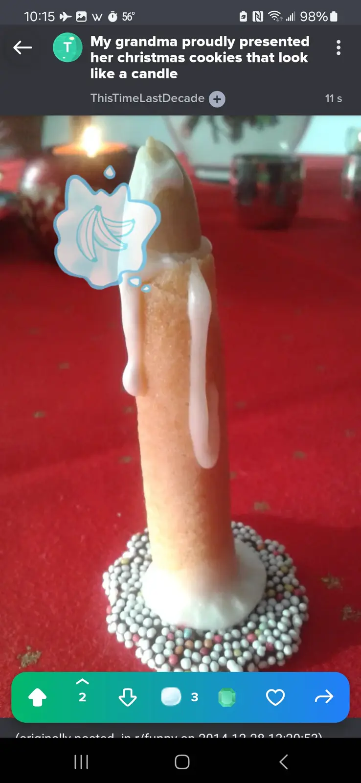 A cookie shaped like a candle with white icing dripping down its sides, standing on a base of colorful sprinkles on a red…