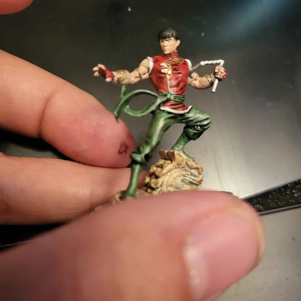 A close-up photo shows a small, painted action figure of the character Ryu from Street Fighter, posed dynamically with…