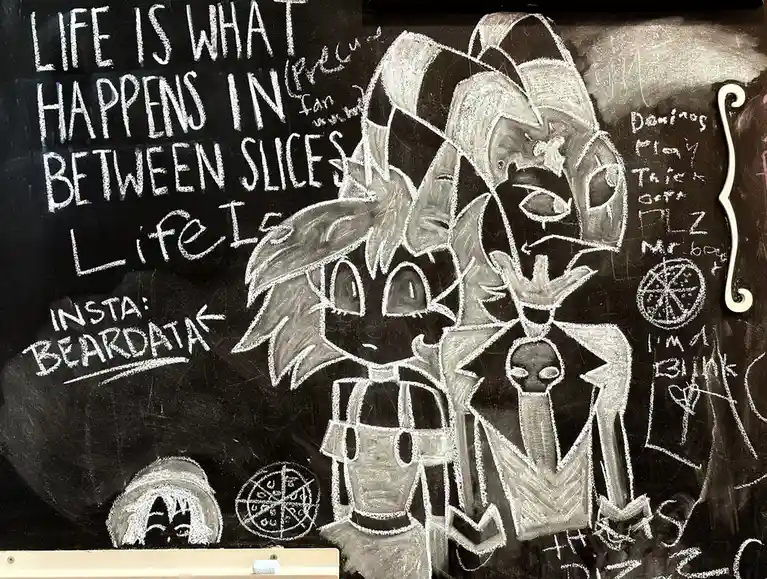 A chalk drawing on a blackboard features two anime-style characters, one with spiky hair and the other with a large hat and…