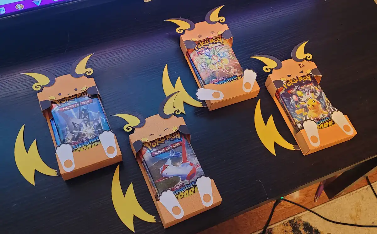 Four Pokémon trading card game booster boxes are creatively decorated to resemble Pikachu, with cutouts for ears, feet, and…