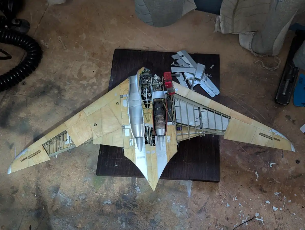 An overhead photo shows a partially assembled model airplane with wooden wings and exposed internal metal framework, sitting…