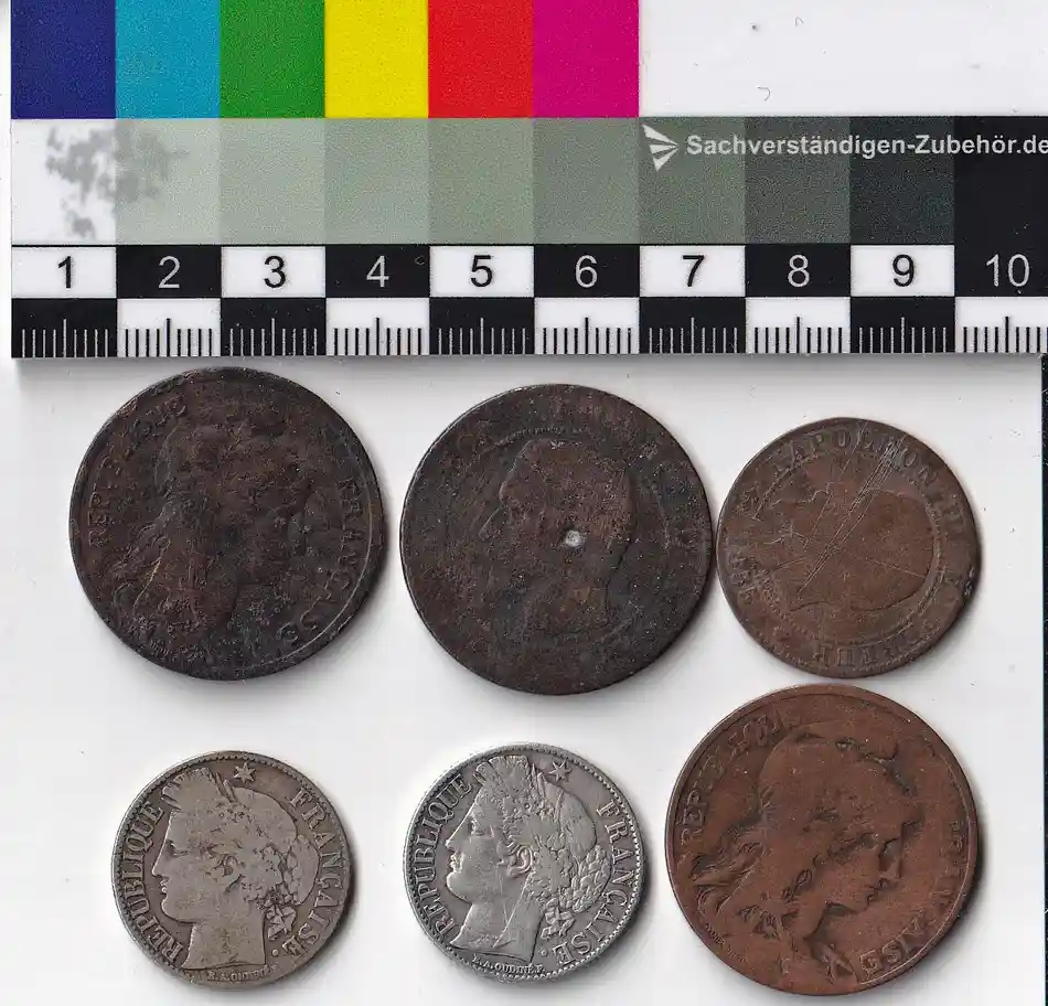 six french coins of varying sizes and designs are laid out on a white surface beneath a ruler and color calibration chart…