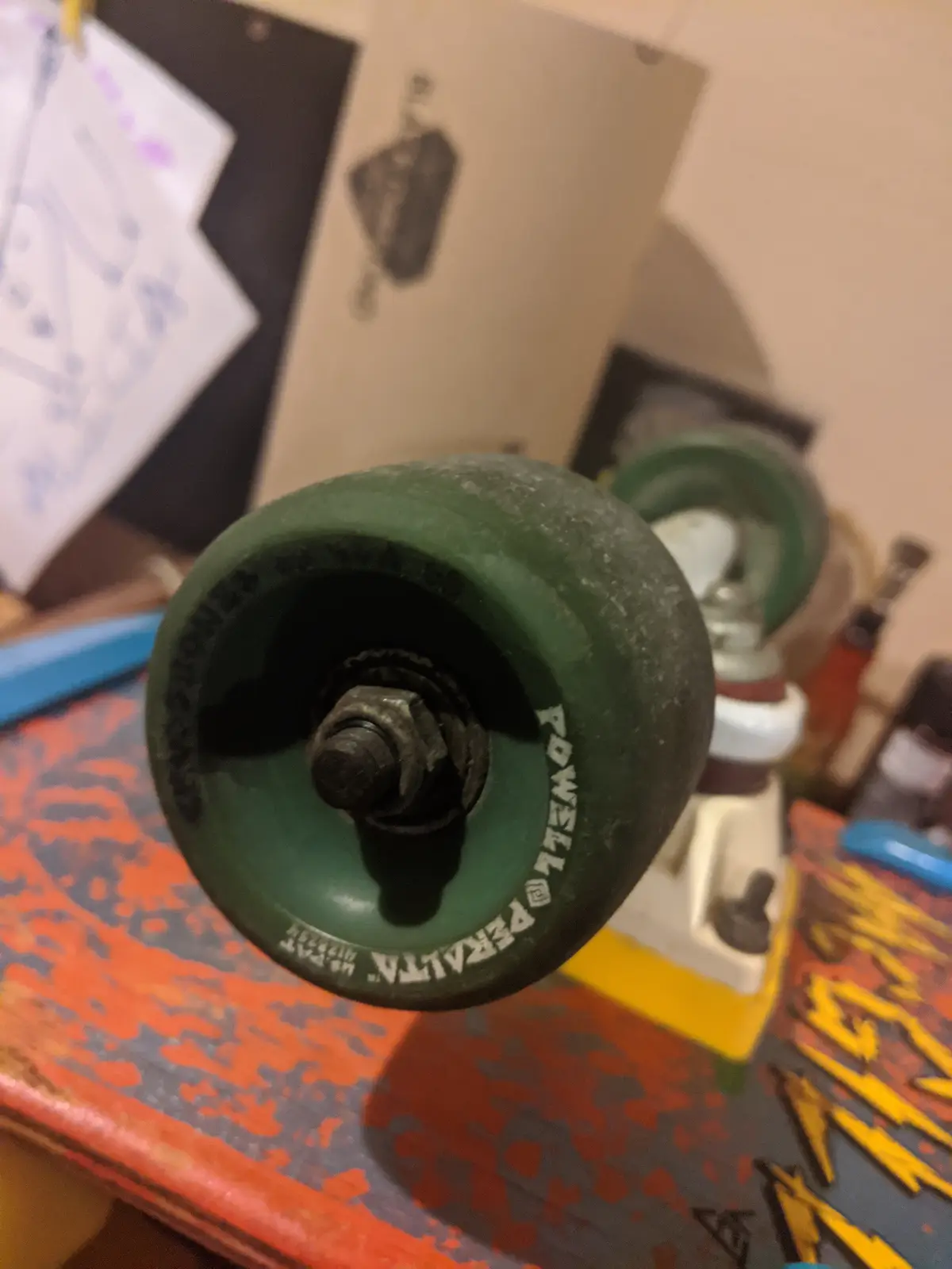 A close-up photo of a worn, dark green skateboard wheel with 'POWELL PERALTA' printed on its side, mounted on a rusty bolt…