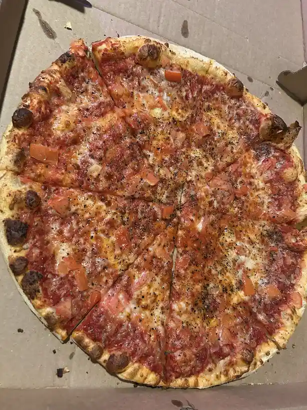 A top-down photo of a freshly baked, sliced pizza in a cardboard box, topped with tomato sauce, melted cheese, diced…