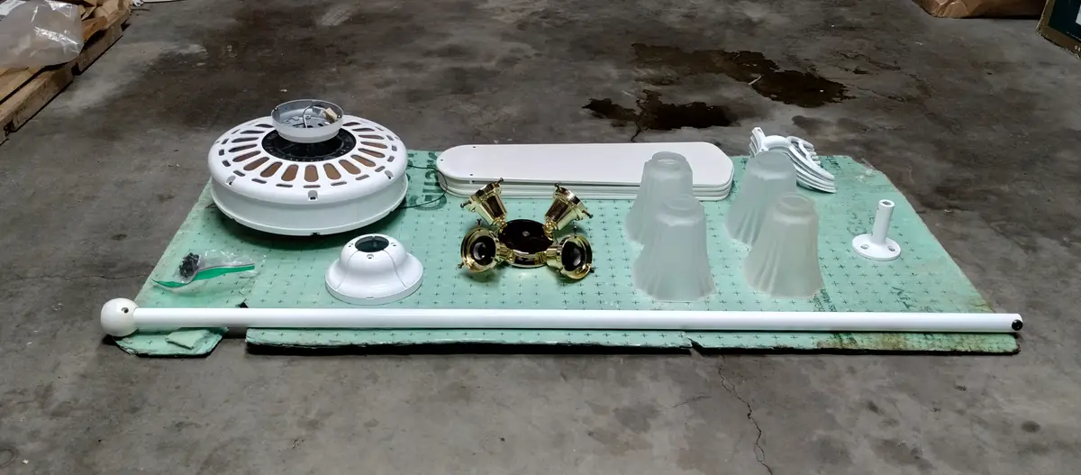 A disassembled ceiling fan and light kit laid out on a green mat on a concrete floor, showing the motor housing, blades…