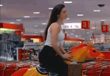 A woman in a white tank top and black pants is shown in a sequence of frames inside a supermarket. In the first three…