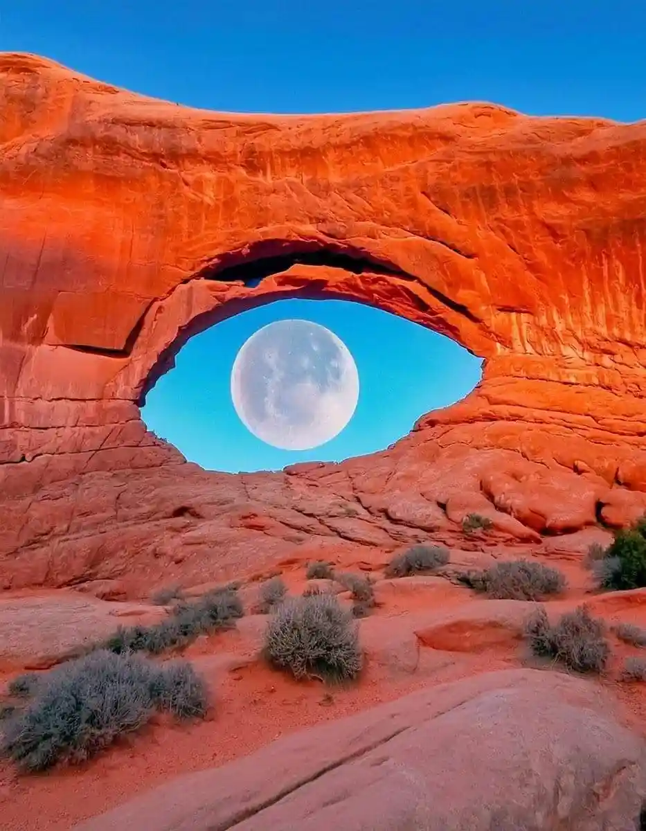 A natural red rock arch frames a full moon against a blue sky, visually resembling an eye. The overlaid text reads 'the moon…