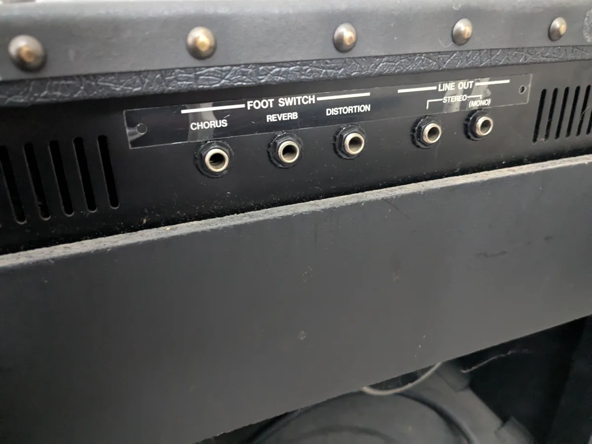 A close-up of a black guitar amplifier's control panel showing labeled footswitch jacks for chorus, reverb, and distortion…