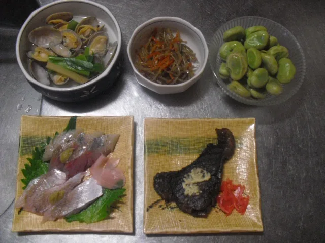 five dishes are arranged on a stainless steel surface: a bowl of clams with green onions, a small bowl of pickled vegetables…