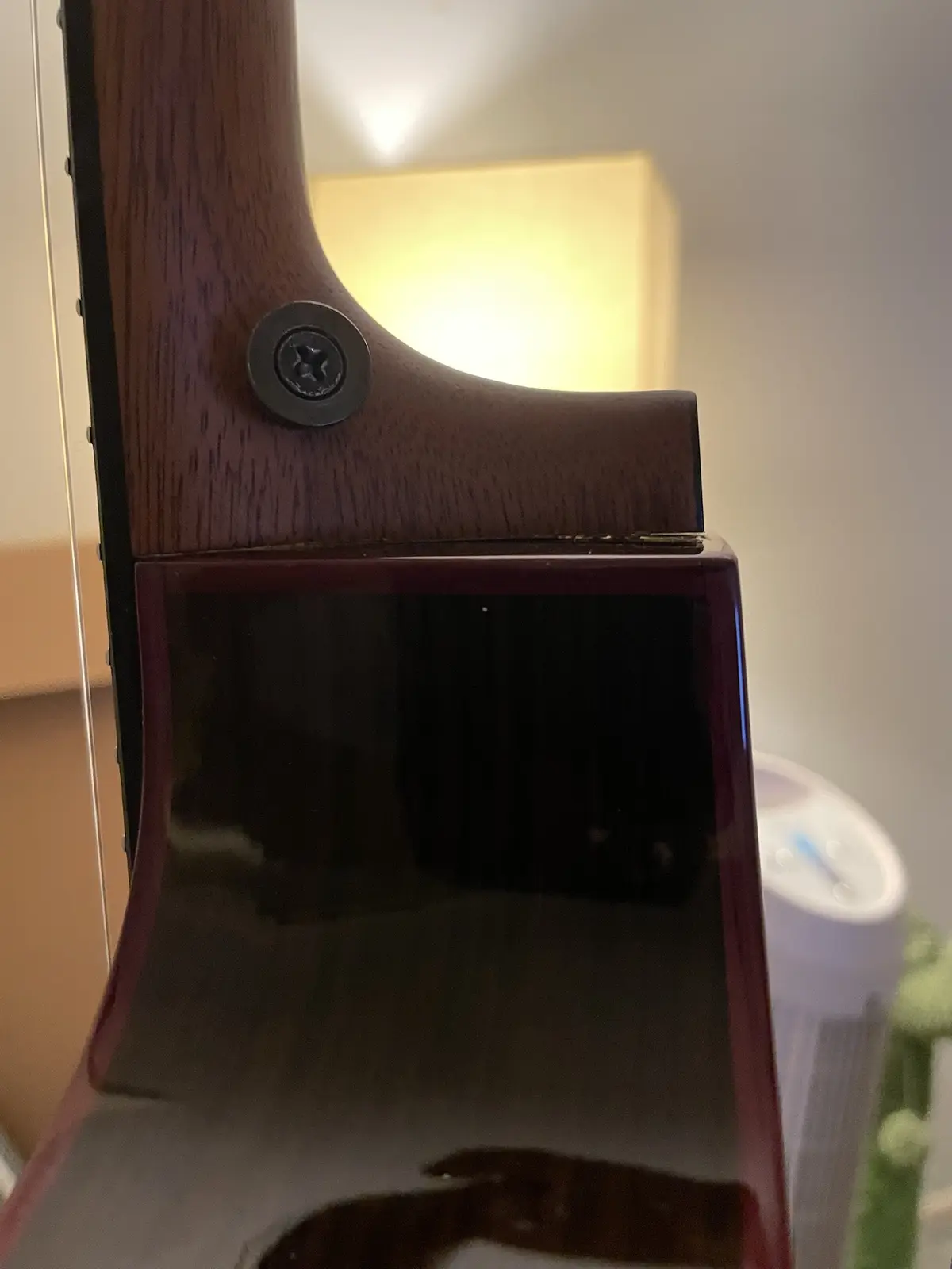 A close-up photo of the back of a guitar's headstock, showing a dark wood finish and a single visible screw. The glossy body…