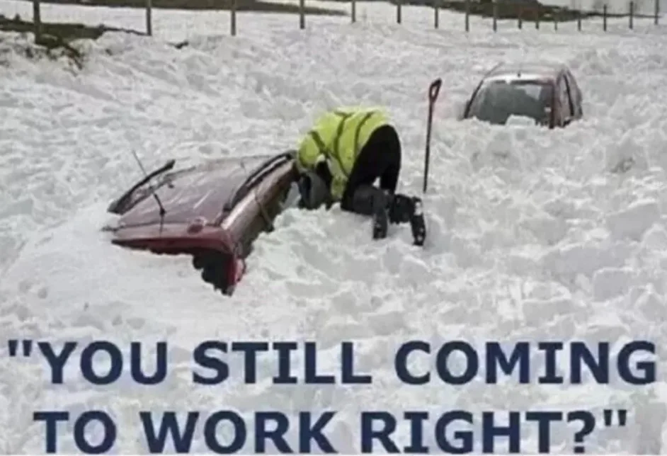 A person in a bright yellow safety vest is kneeling in deep snow next to a red car that is almost completely buried. Another…