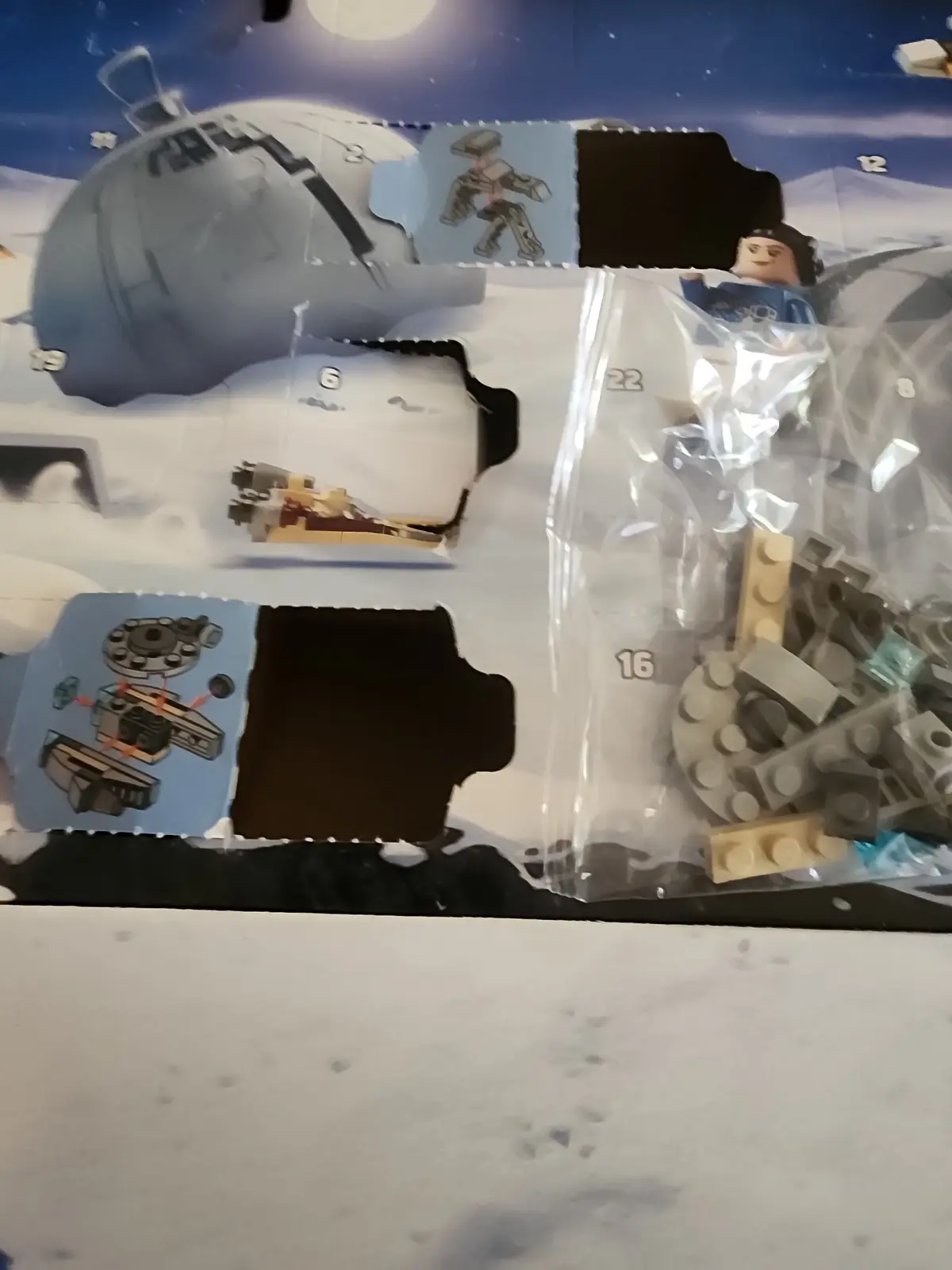 A close-up of a partially opened LEGO set box showing the instruction booklet with numbered steps and cut-out compartments…