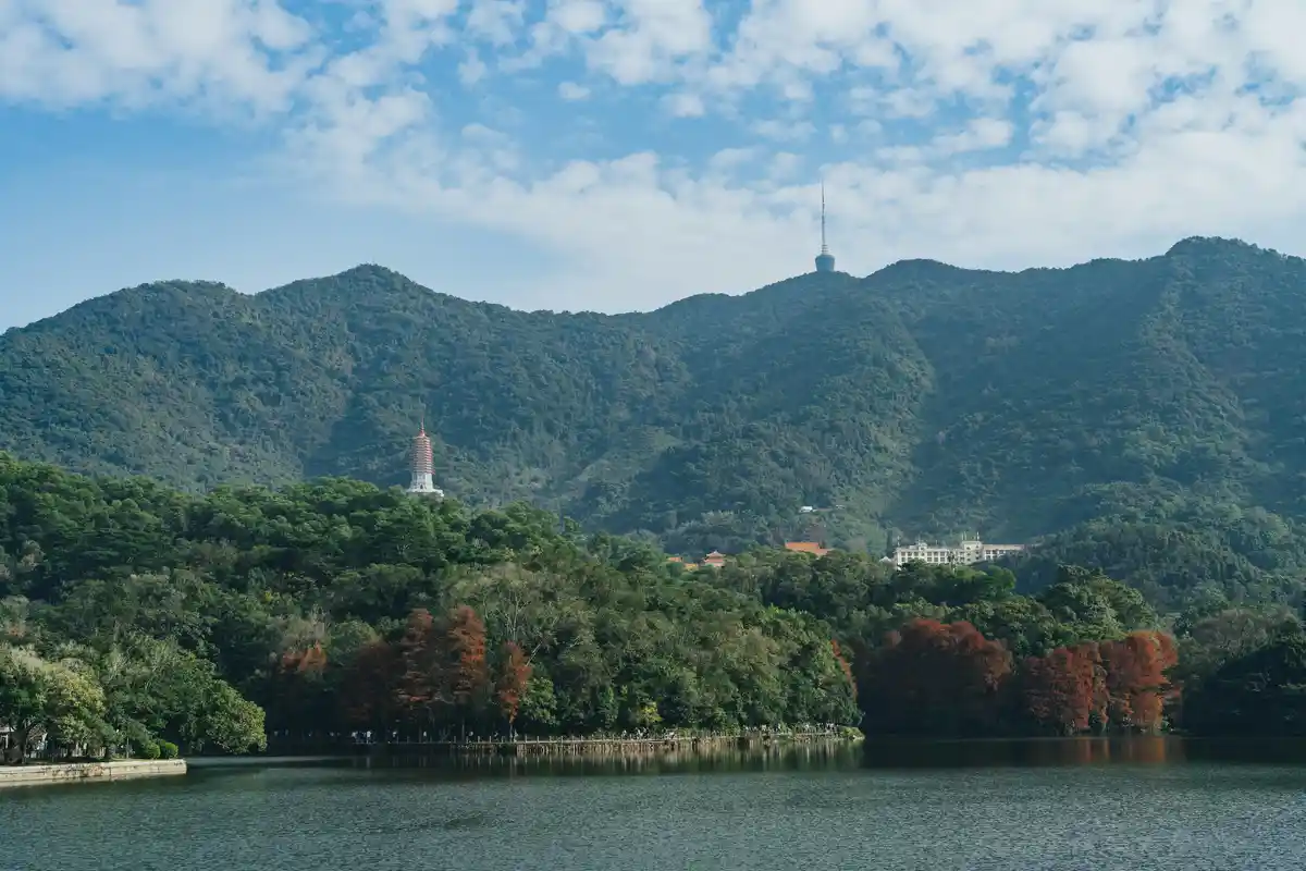 A scenic landscape photo shows a calm lake in the foreground with a forested mountain range in the background. On the left…