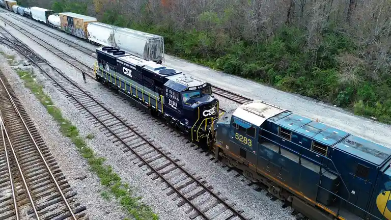 An aerial photo shows two CSX trains on parallel tracks, with one locomotive (number 911343) positioned to push or pull the…