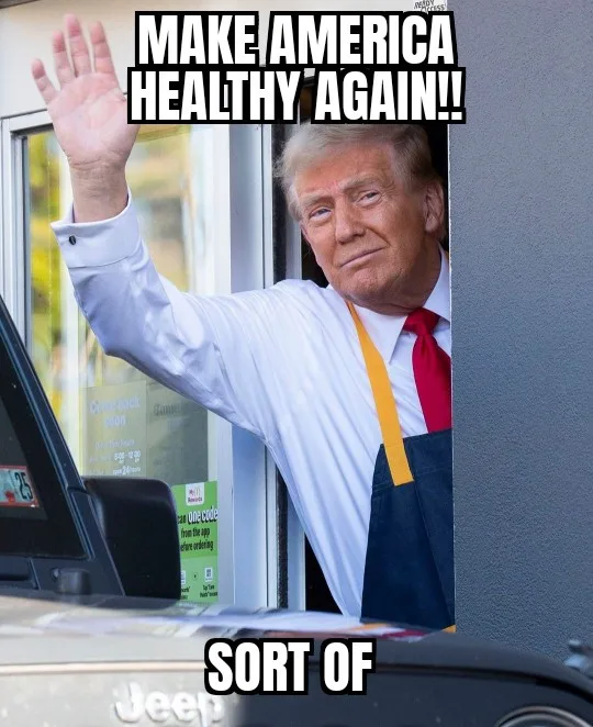 A man with blond hair wearing a white shirt, red tie, and blue apron waves from a drive-thru window. The text overlaid at…