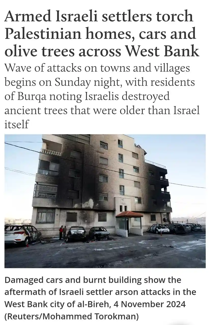 The image shows a multi-story building with visible fire damage on its facade, alongside several burnt-out cars in a parking…