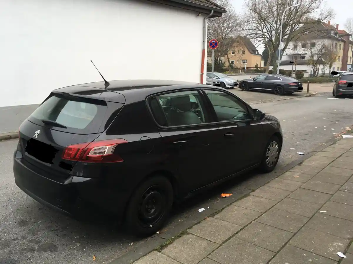 A black Peugeot 207 hatchback is parked on a street next to a sidewalk, with its rear passenger-side wheel missing and…