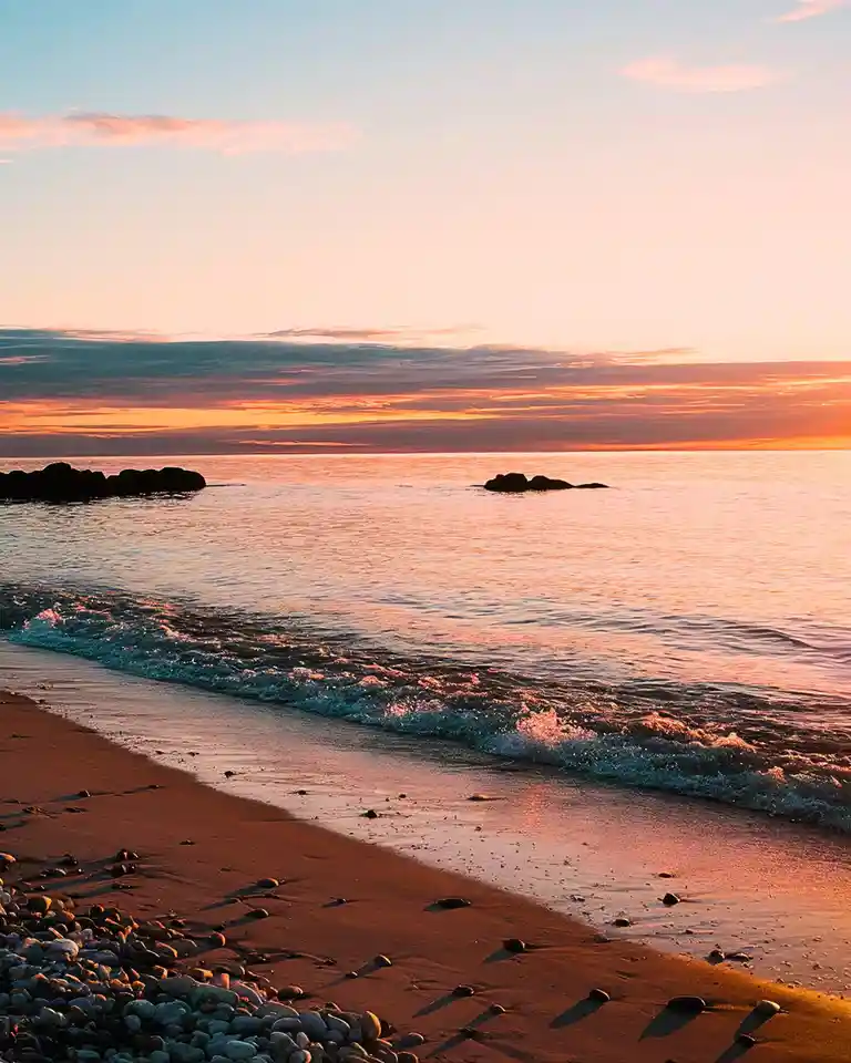 A serene beach scene at sunset with calm waters, orange and pink sky, and rocks along the shore. Overlaid text reads 'i'm…