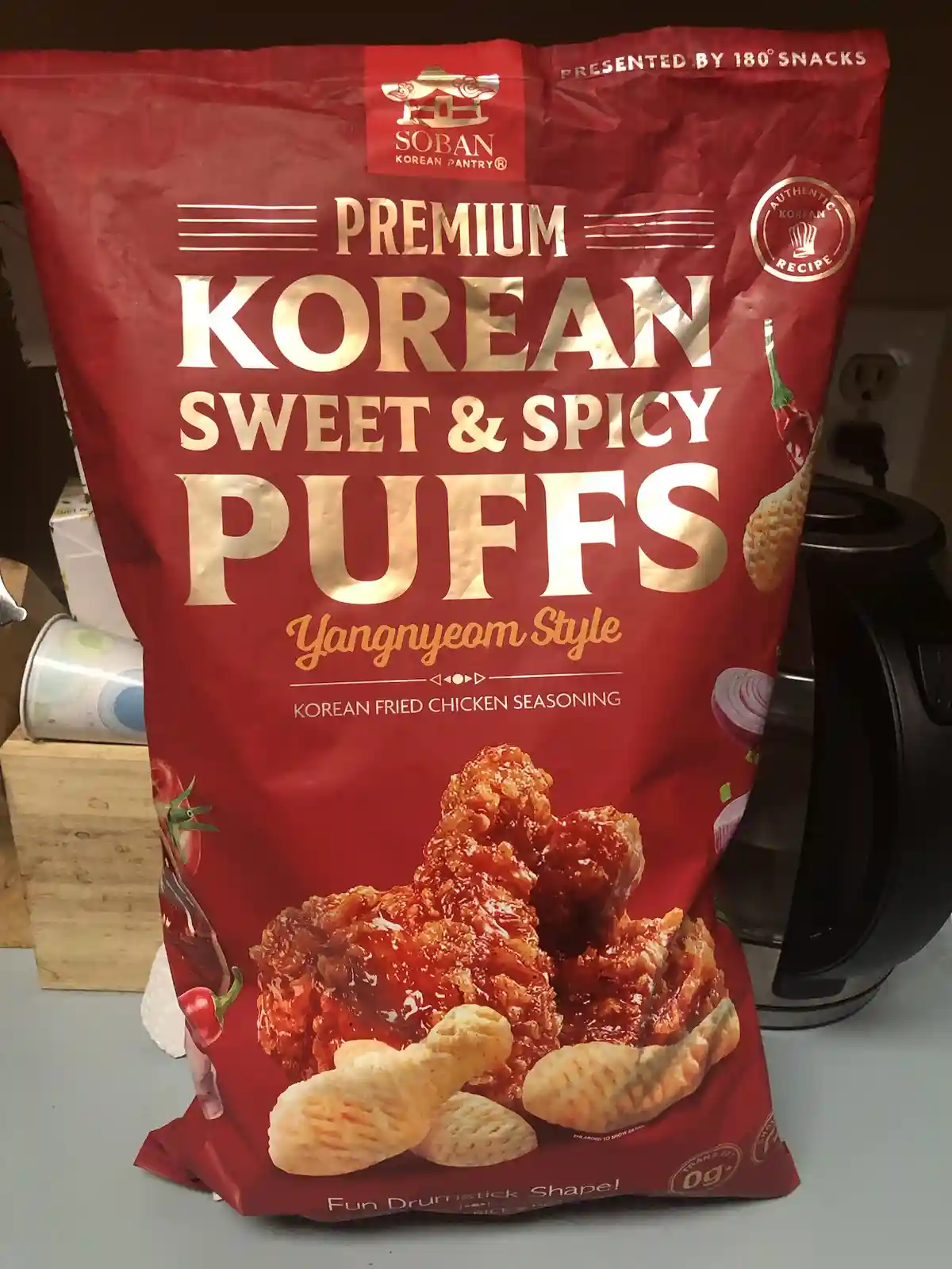 A red bag of Soban Korean Pantry Premium Sweet & Spicy Puffs, styled like Yangnyeom fried chicken, sits on a kitchen…